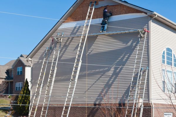 Workers installing plastic siding panels on two story house.